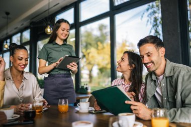 Garsondan yemek sipariş eden bir grup insan. Garson tablete emirler yazıyor. Garson onlara yardım ederken kararsız insanlar menüyü okuyor..