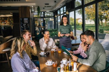 Garsondan yemek sipariş eden bir grup insan. Garson tablete emirler yazıyor. Garson onlara yardım ederken kararsız insanlar menüyü okuyor..