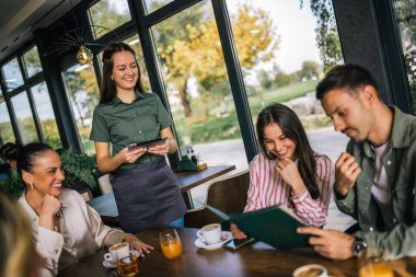 Garsondan yemek sipariş eden bir grup insan. Garson tablete emirler yazıyor. Garson onlara yardım ederken kararsız insanlar menüyü okuyor..