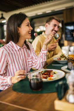 Bir grup mutlu arkadaş birlikte bir restoranda öğle yemeği yiyorlar. Lezzetli salatalar, hamburgerler, ekmek ve et yerler..