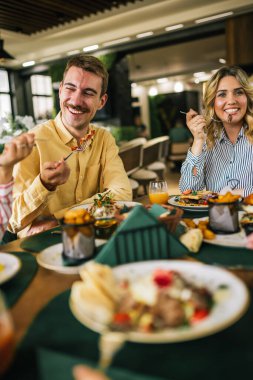 Bir grup mutlu arkadaş birlikte bir restoranda öğle yemeği yiyorlar. Lezzetli salatalar, hamburgerler, ekmek ve et yerler..