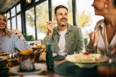Bir grup mutlu arkadaş birlikte bir restoranda öğle yemeği yiyorlar. Lezzetli salatalar, hamburgerler, ekmek ve et yerler..