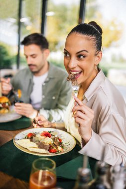 Güzel bir kadın arkadaşlarıyla bir restoranda öğle yemeği yer. Salatayla et yiyor..