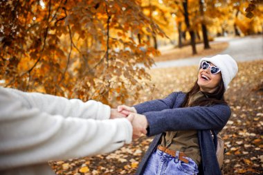 Genç mutlu çift, güneşli bir sonbahar gününde el ele tutuşup renkli parkta yürüyor..