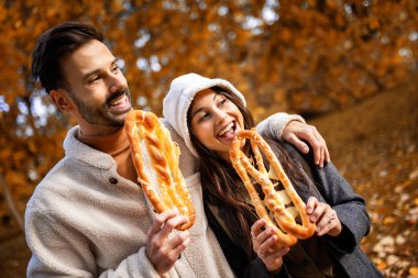 Genç bir çift, sonbahar günü renkli bir parkta simit yiyor..