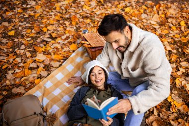 Genç tatlı çift piknik yapar ve renkli bir sonbahar parkında birlikte kitap okurlar..