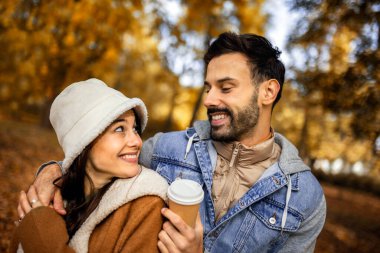 Parkta kahve içen genç bir çift. Parktaki renkli sonbahar titreşimleri. Sarılmak, yürümek ve el ele tutuşmak..