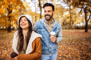 Parkta kahve içen genç bir çift. Parktaki renkli sonbahar titreşimleri. Sarılmak, yürümek ve el ele tutuşmak..