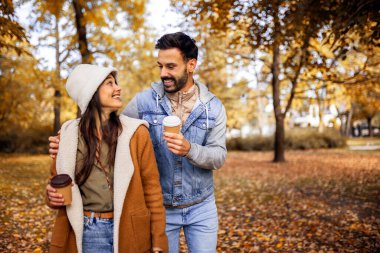 Parkta kahve içen genç bir çift. Parktaki renkli sonbahar titreşimleri. Sarılmak, yürümek ve el ele tutuşmak..