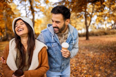 Parkta kahve içen genç bir çift. Parktaki renkli sonbahar titreşimleri. Sarılmak, yürümek ve el ele tutuşmak..