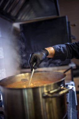 Mutfakta aşçı büyük tencerede yeşil bezelye, biftek, patates, soslu soğan pişiriyor..