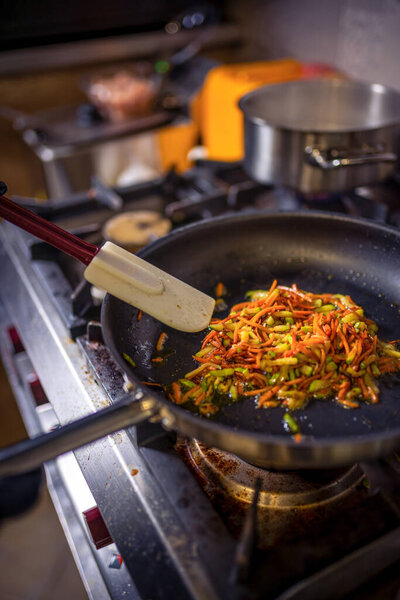 Шеф-повар жарит овощи на сковородке на кухне ресторана.