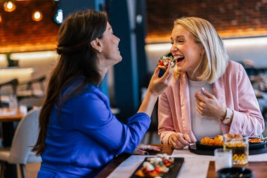 Restoranda birbirini besleyen gülümseyen lezbiyen çift.