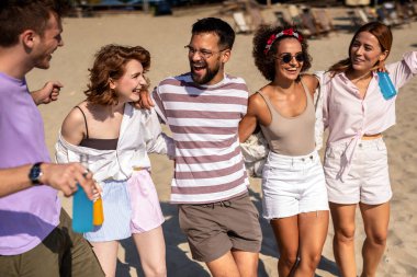 Bir grup arkadaş sahilde birlikte yürüyorlar. Renkli kokteyller içip eğleniyorlar..