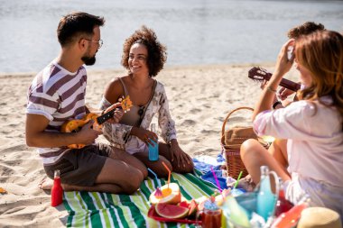 Arkadaşlar plajda piknik yapıyor. Ukulele çalıyorlar, kokteyl içiyorlar, takılıyorlar..