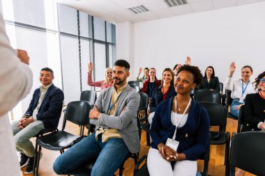 Erkek CEO, çok ırklı bir grup meslektaşın önünde duruyor ve soruyu cevaplaması için birini çağırıyor. Akıllı tahtası olan çokluortam sınıfı.