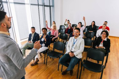 Erkek CEO, çok ırklı bir grup meslektaşın önünde duruyor ve soruyu cevaplaması için birini çağırıyor. Akıllı tahtası olan çokluortam sınıfı.