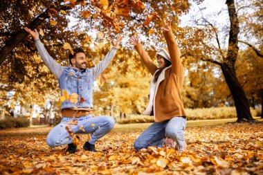 Genç mutlu çift parkta sarılıyor, yürüyor ve yaprak fırlatıyor. Güneşli sonbahar gününde Renkli park.