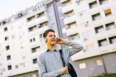 Kulağında kulaklıkla şehir caddesinde yürüyen genç bir çocuk. 