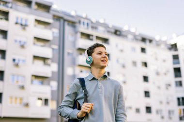 Kulağında kulaklıkla şehir caddesinde yürüyen genç bir çocuk. 