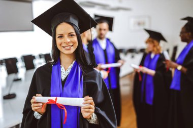 Arkadaşlarının önünde diplomasını tutan Toga 'lı bir öğrencinin portresi..