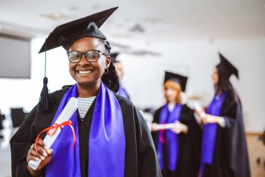Toga giyip arkadaşlarının önünde diplomasını tutan Afrikalı Amerikalı bir öğrencinin portresi..
