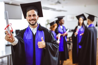 Arkadaşlarının önünde diplomasını tutan Toga 'lı bir öğrencinin portresi..