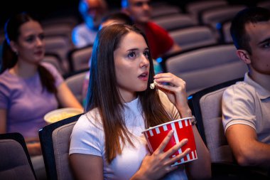 Girl is eating popcorn and watching a movie in the cinema.