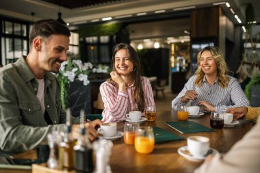 Bir grup genç, modern bir kafede bir masada oturup bir fincan kahve ve taze sıkılmış meyve suyuyla eğleniyorlar..