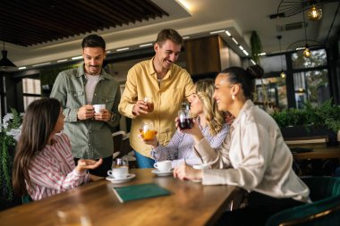 İki genç adam bir kafede bir grup kadına yaklaşıyorlar, dostça sohbet ediyorlar.