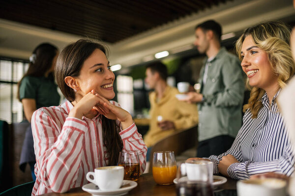 Group of female friends drinking coffee at the restaurant while the guys in the back try to flirt and send them drinks.
