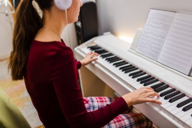 Rahat odasında piyano çalarken kulaklık takan genç bir kadın, müziğine derinden odaklanmış..