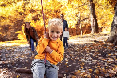 Mutlu aile sonbahar parkında salıncakta sallanırken eğleniyor.