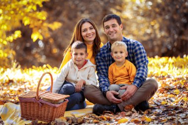 Mutlu bir aile ve iki küçük oğlu parkta rahat bir sonbahar pikniği yapıyorlar.