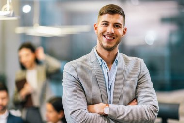 Meslektaşlarının önünde kollarını kavuşturmuş genç ve yakışıklı iş adamının portresi..