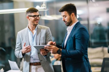Koridorda konuşan iki meslektaş. İş için tablet kullanılıyor.
