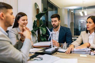 Parlak insanlar sürdürülebilir enerjiden bahsediyorlar. Masada yel değirmeni var ve dizüstü bilgisayarla çalışıyorlar..
