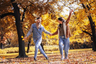 Mutlu çift bir sonbahar günü renkli parka yapraklar fırlatıyor..