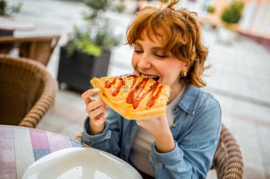Genç kızıl kız bir dilim lezzetli pizzayı ısırıyor..
