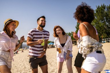 Bir grup çok ırklı arkadaş sahilde eğleniyor. Dans eder, zıplar ve kokteyl içerler..