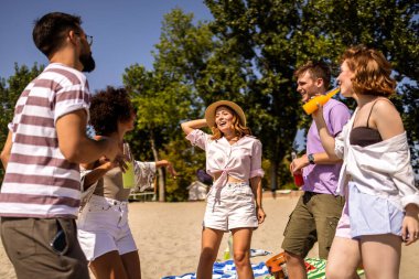 Bir grup çok ırklı arkadaş sahilde dans ederken kokteyl içip müzik dinliyorlar..