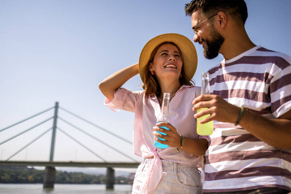 Couple on the beach looking at each other. They hold cocktails in their hands.