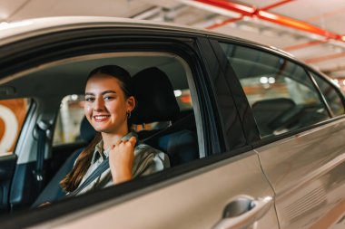 Genç iş kadını emniyet kemeri takıyor. Bir yeraltı garajındaki park yerinden uzaklaşmaya hazır..