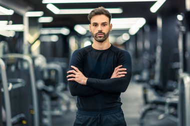 Spor salonunda kolları çapraz duran kaslı fitness adamı..