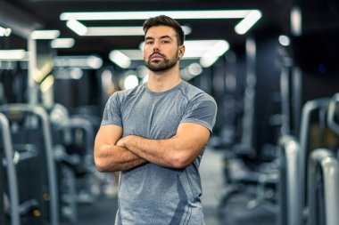 Spor salonunda kolları çapraz duran kaslı fitness adamı..