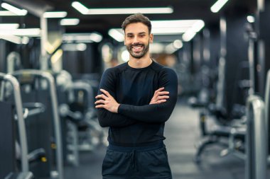 Spor salonunda kolları çapraz duran kaslı fitness adamı..