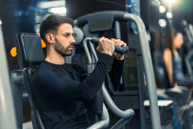 Sportif adam spor salonunda kol presi makinesinde egzersiz yapıyor..