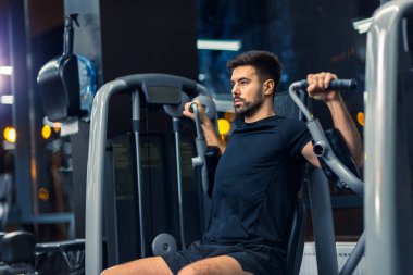 Sportif adam spor salonunda kol presi makinesinde egzersiz yapıyor..