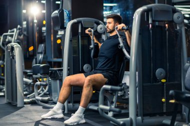 Sportif adam spor salonunda kol presi makinesinde egzersiz yapıyor..