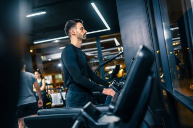 Genç yakışıklı adam spor salonunda koşu bandında koşuyor..
